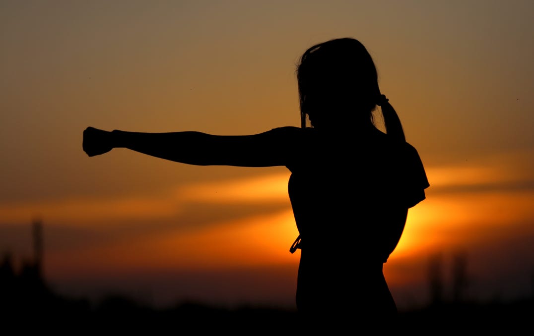 Silhouette of a girl, throwing a punch with a background of a sunset